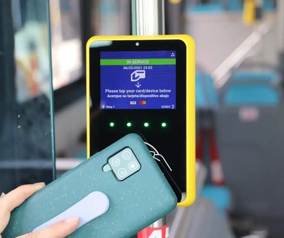 A green android smartphone is held next to the yellow and black payment reader whose screen says "in service".