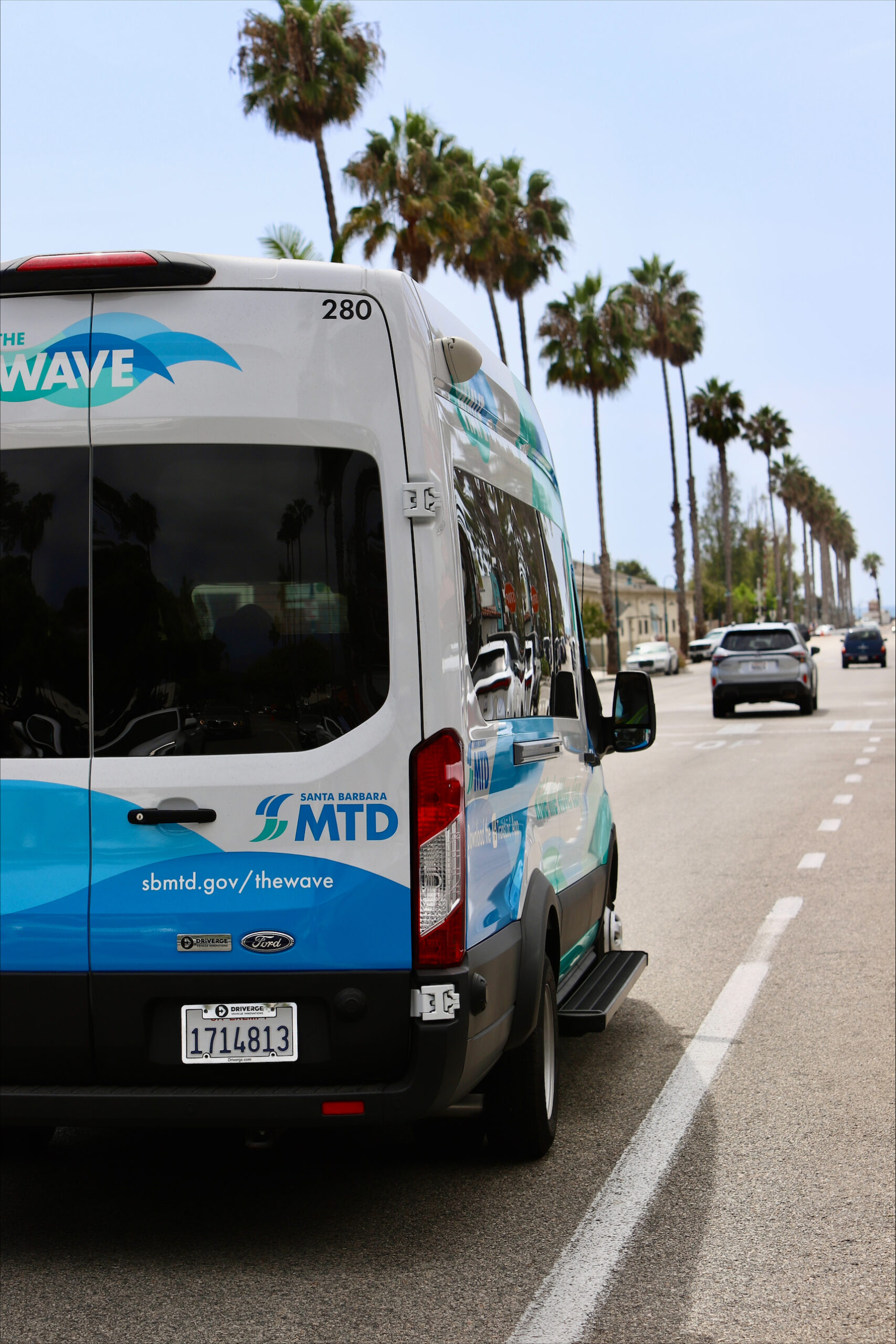 A photo of the back of The Wave van coasting down a palm tree lined street in Capinteria on a sunny day.